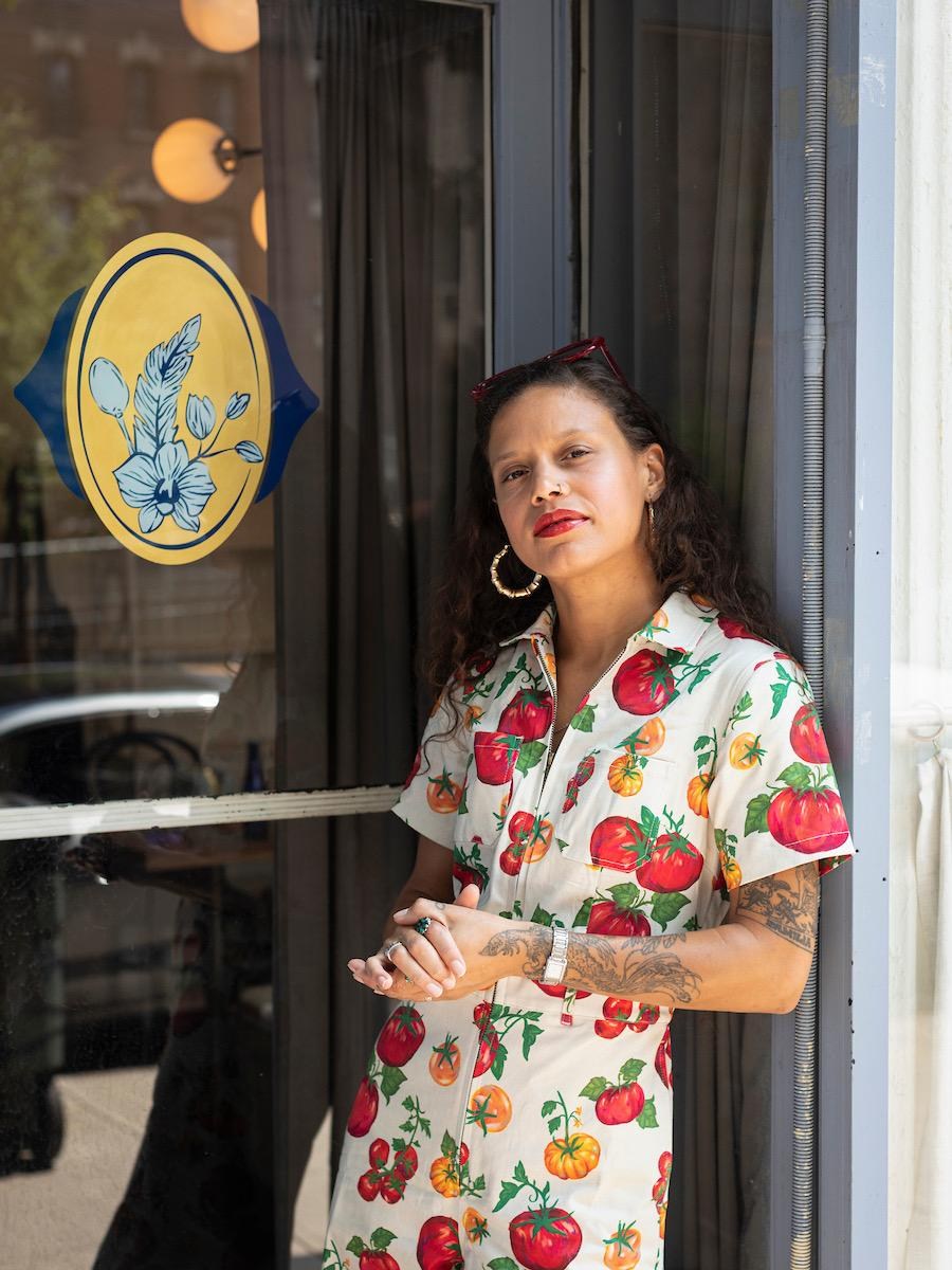 A woman in a bright jumpsuit leaning against the window of a restaurant.