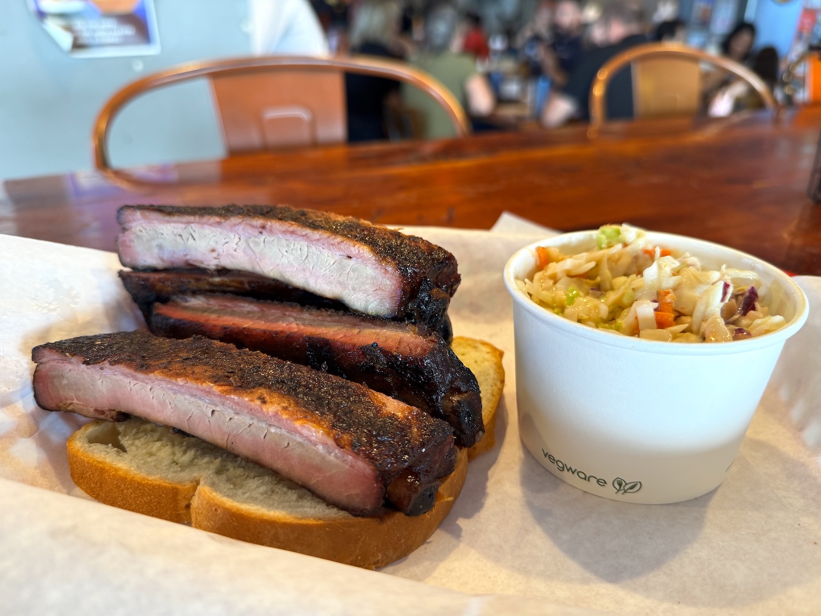 Smoked pork ribs piled on a slice of white bread with a side of coleslaw in a paper cup.
