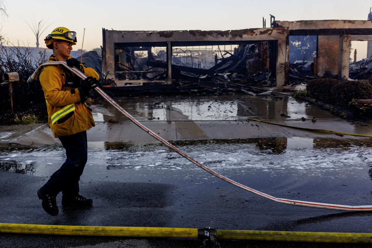 A firefighter wraps up his hose after the Norte fire destroyed homes on Via La Mirada on Friday in San Juan Capistrano.