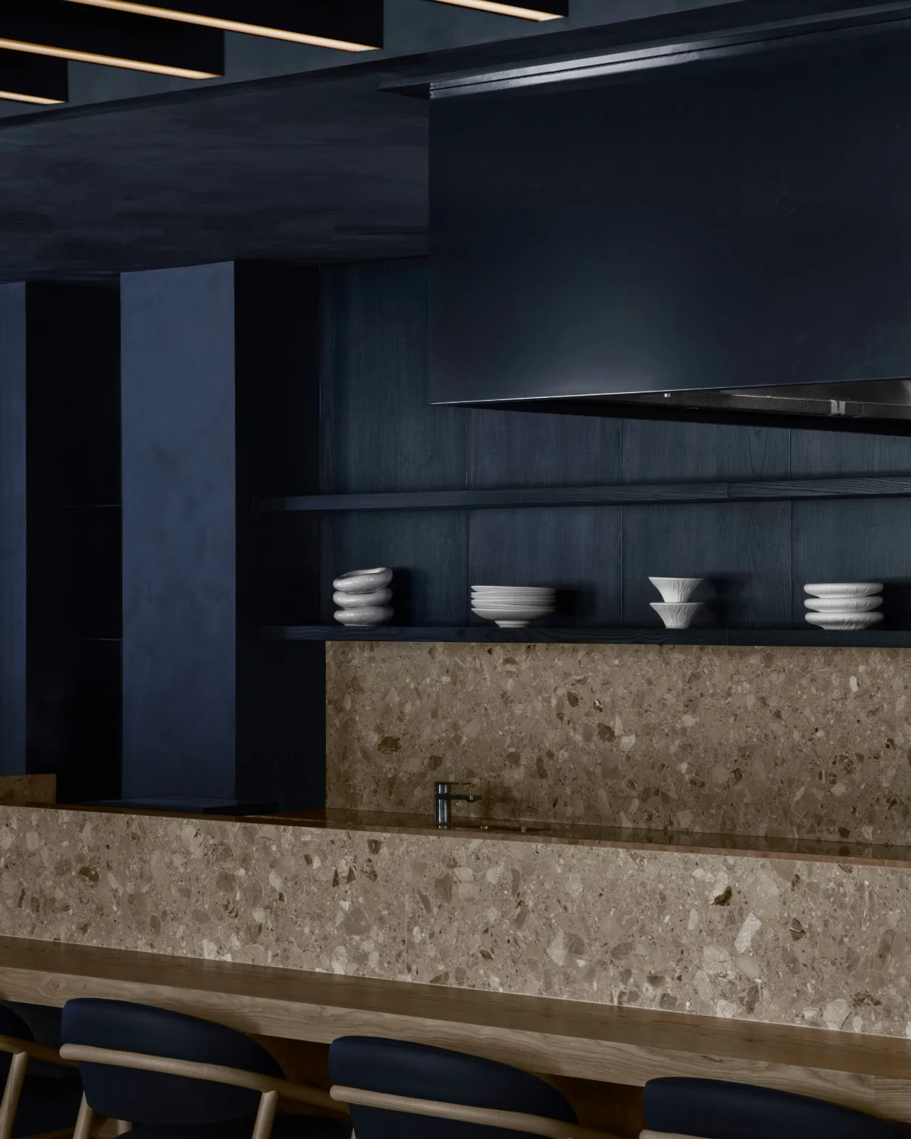 Japanese steakhouse kitchen bar with beige stone backsplash and a shelf of white bowls.