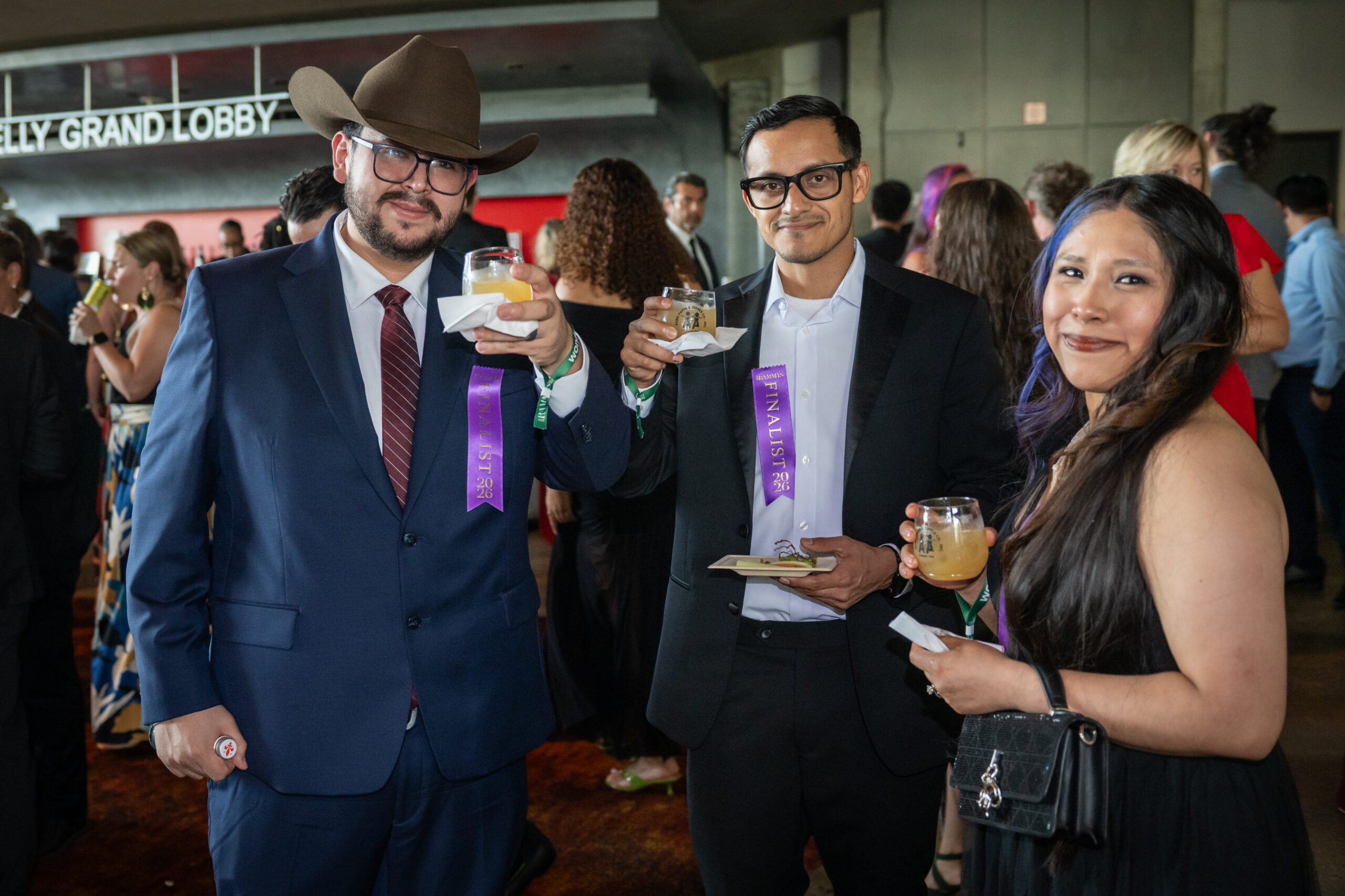 Three RAMMY Awards attendees, including two wearing purple finalist ribbons, pose with drinks during the 2026 RAMMY celebration at The Wharf.