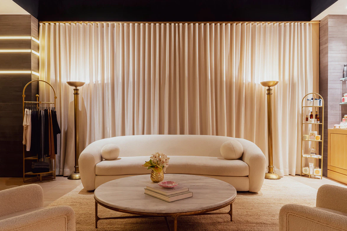 Modern living room with a white sofa, round coffee table, and floor lamps against closed beige curtains.