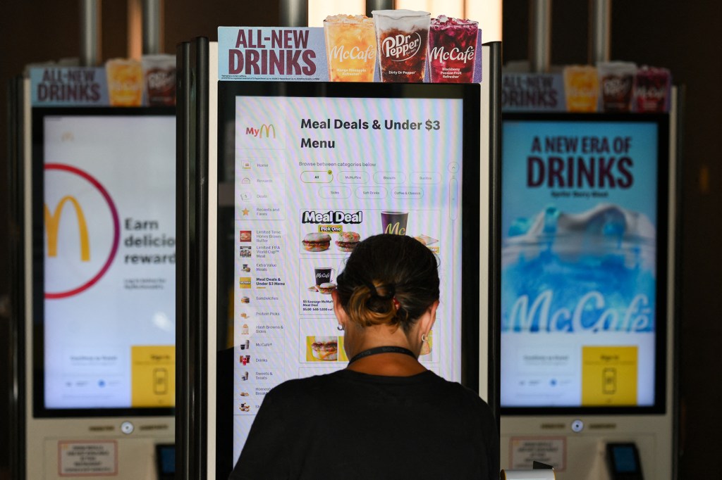 A person ordering from a McDonald's self-service kiosk showing "Meal Deals & Under $3" on the menu.