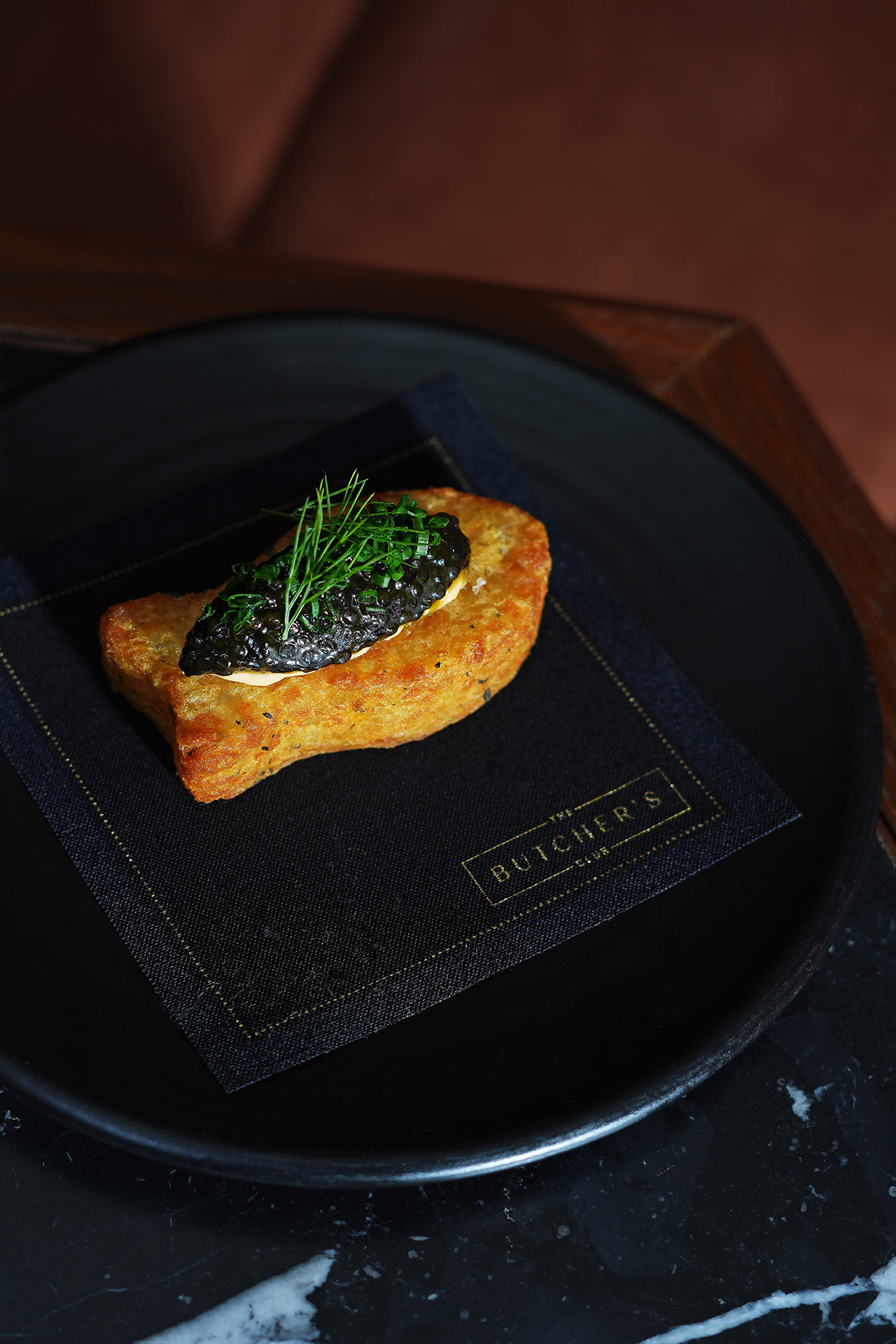 A hash brown is cut into the shape of “one fish,” while a topping of smoked salmon crème fraîche and caviar delivers the “two fish.” © The Butcher's Club