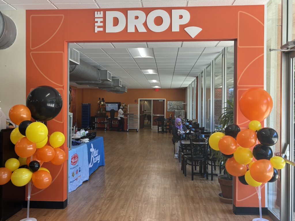 Entrance to The Drop decorated with orange, black, and yellow balloons, leading to a room with tables and chairs.