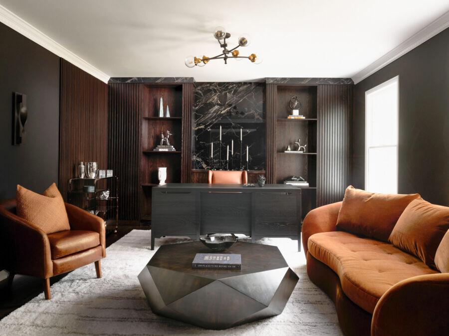 Inside a colonial home in Randolph, NJ, lush textures, sculptural lighting and organic forms soften the masculine edge of this moody home office, equally suited to work, game days and unwinding with friends. Polished Galaxy porcelain sets a dramatic backdrop for bespoke built-ins, while flanking fluted panels hide integrated doors.