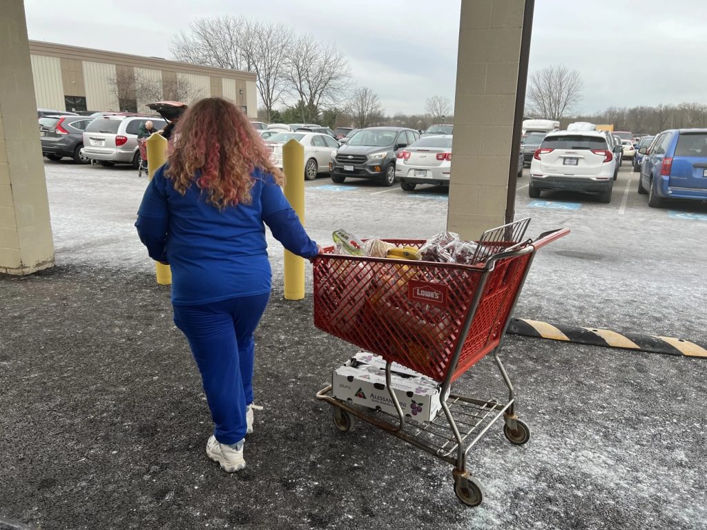 A woman pulls a shopping cart full of groceries from the front.
