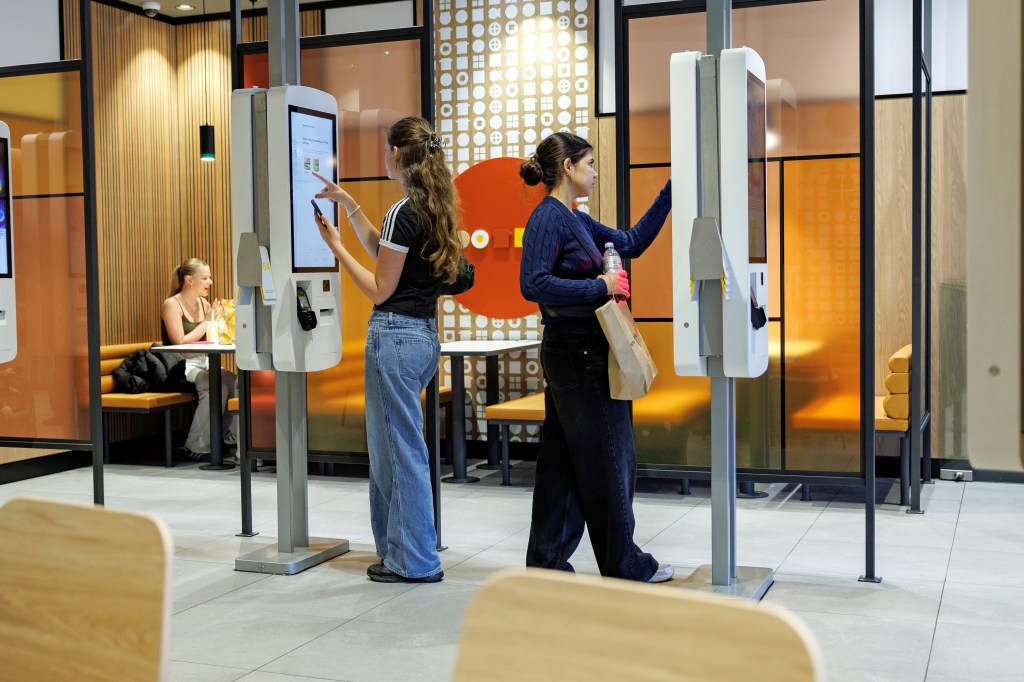Two young women ordering food at self-service kiosks in a McDonald's branch.