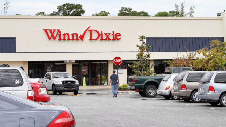 Shopper walks through cars parked outside a Winn-Dixie location entrance