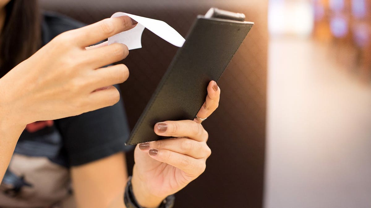 A woman whose face can't be seen reviews a restaurant's food bill.