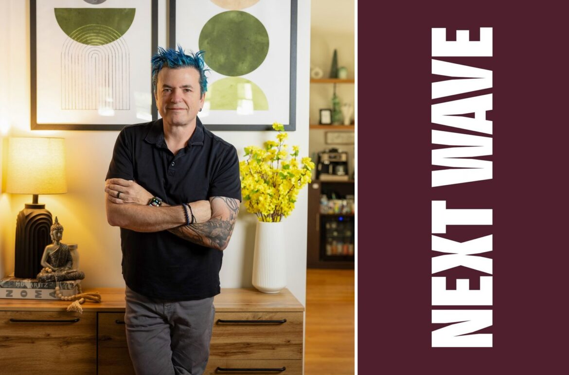 Jason Santos Brings Citrus & Salt to His Burlington Community Jason Santos stands with his arms crossed in a restaurant beside vertical Next Wave lettering on maroon.