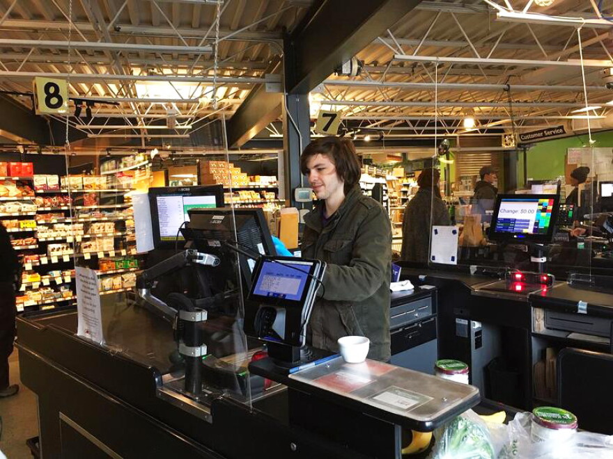 A person at a cash register with a sheet of plexiglass.
