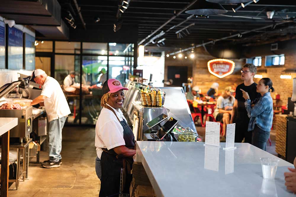 Employee in a pink cap and apron smiling behind the counter at The Franklin Butchery in Franklin, TN