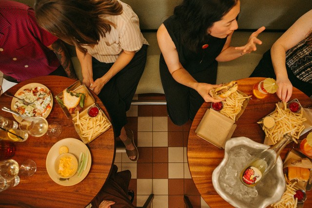 An overhead image of two tables of diners with wine and fries and burgers.