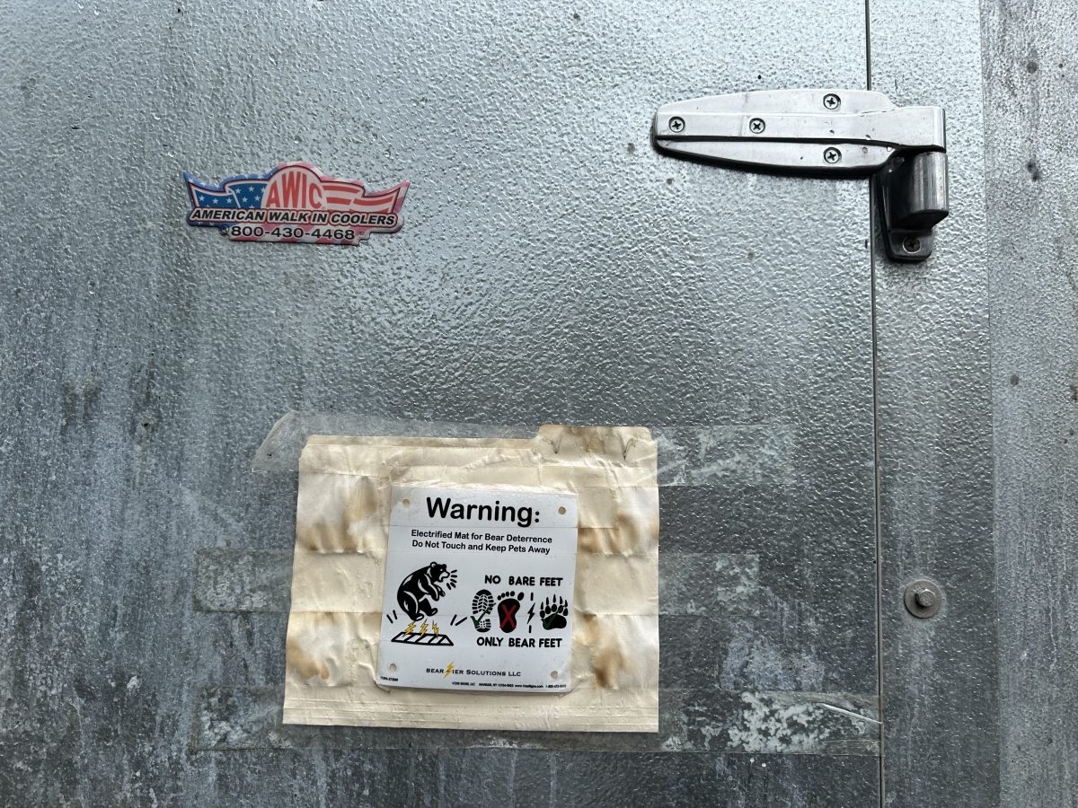 Metal door with an “American Walk-In Coolers” sticker and a taped warning sign stating “No Bare Feet, Only Bear Feet” with illustrated animal footprints below.
