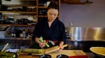 A sushi chef grates green wasabi rhyzome in a kitchen.