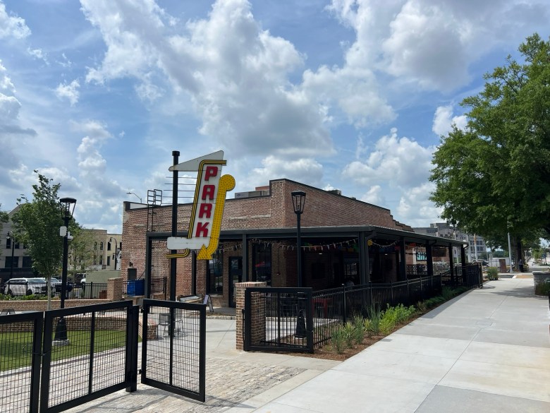 Exterior of Founder's Park and a restaurant in South Downtown Atlanta with retro vertical sign, covered patio, and brick facade along a sidewalk.