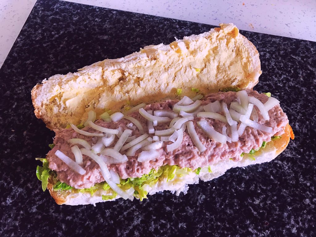 Tuna salad in a cheese sub on a bed of iceberg lettuce with white onion topping.