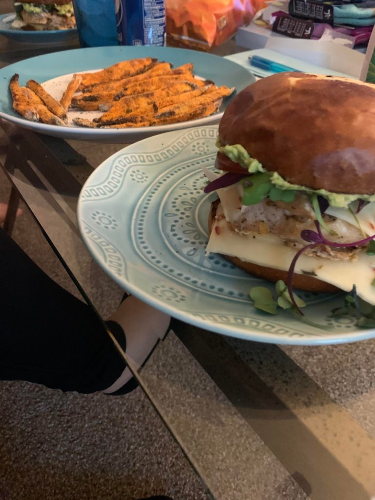 Grilled chicken sandwich on a toasted pretzel bun, and homemade sweet potato fries