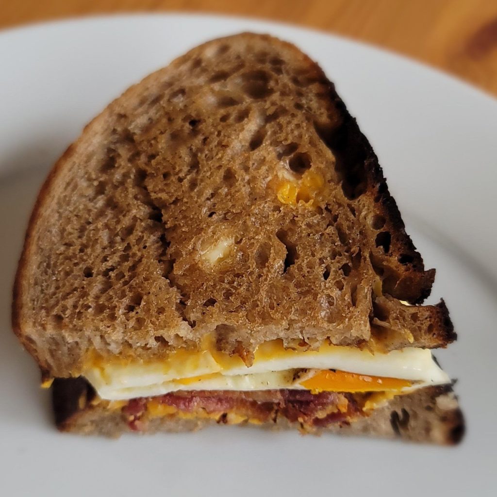 Sourdough Breakfast Sandwich: Homemade Sourdough toasted on the inside and dressed with mayo. Stacked with American Cheese, Eggs Over Medium, and Thick Cut Bacon.