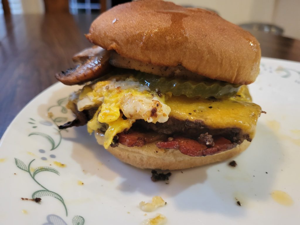 Breakfast supreme burger: Keto bun, fried eggs, sauteed mushrooms, bacon, spicy garlic aioli, pickles, and two patties.