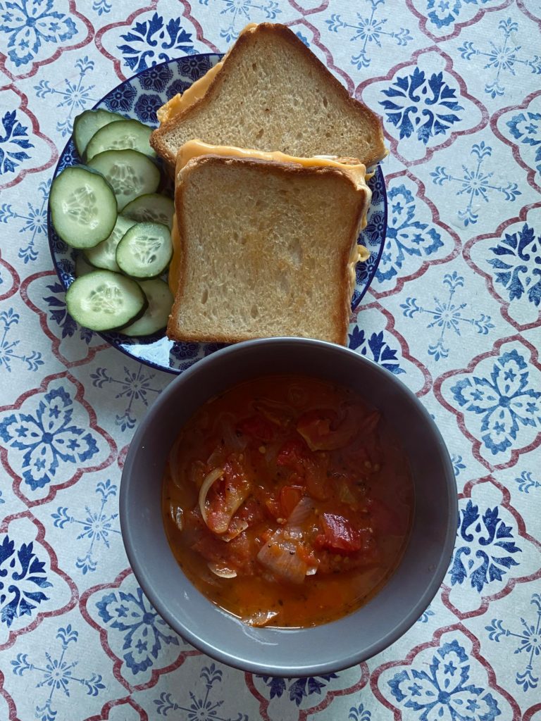 Grilled cheese sandwiches and chunky tomato soup with a side of cucumber slices
