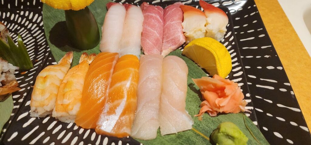 a variety of nigiri and a roll topped with albacore and garlic