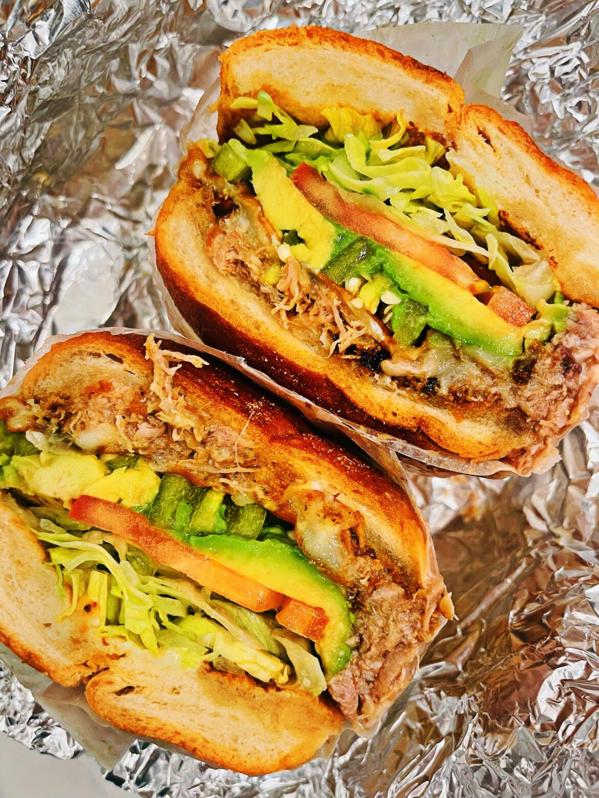Torta de carnitas with pinto beans, jalapeños, lettuce, tomato, onion, and avocado