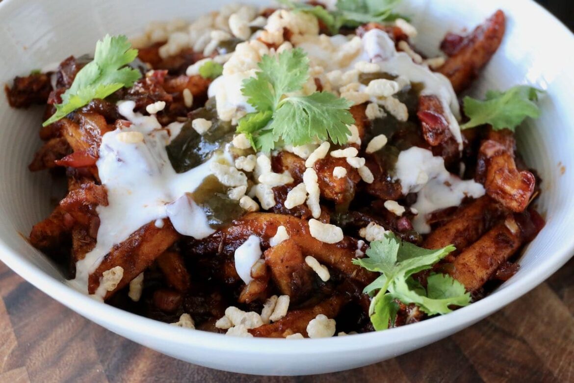 Vegetarian Masala Chips feature crispy baked French Fries tossed in a spicy Indian Masala curry sauce. Garnished with cilantro, puffed rice and tamarind chutney.