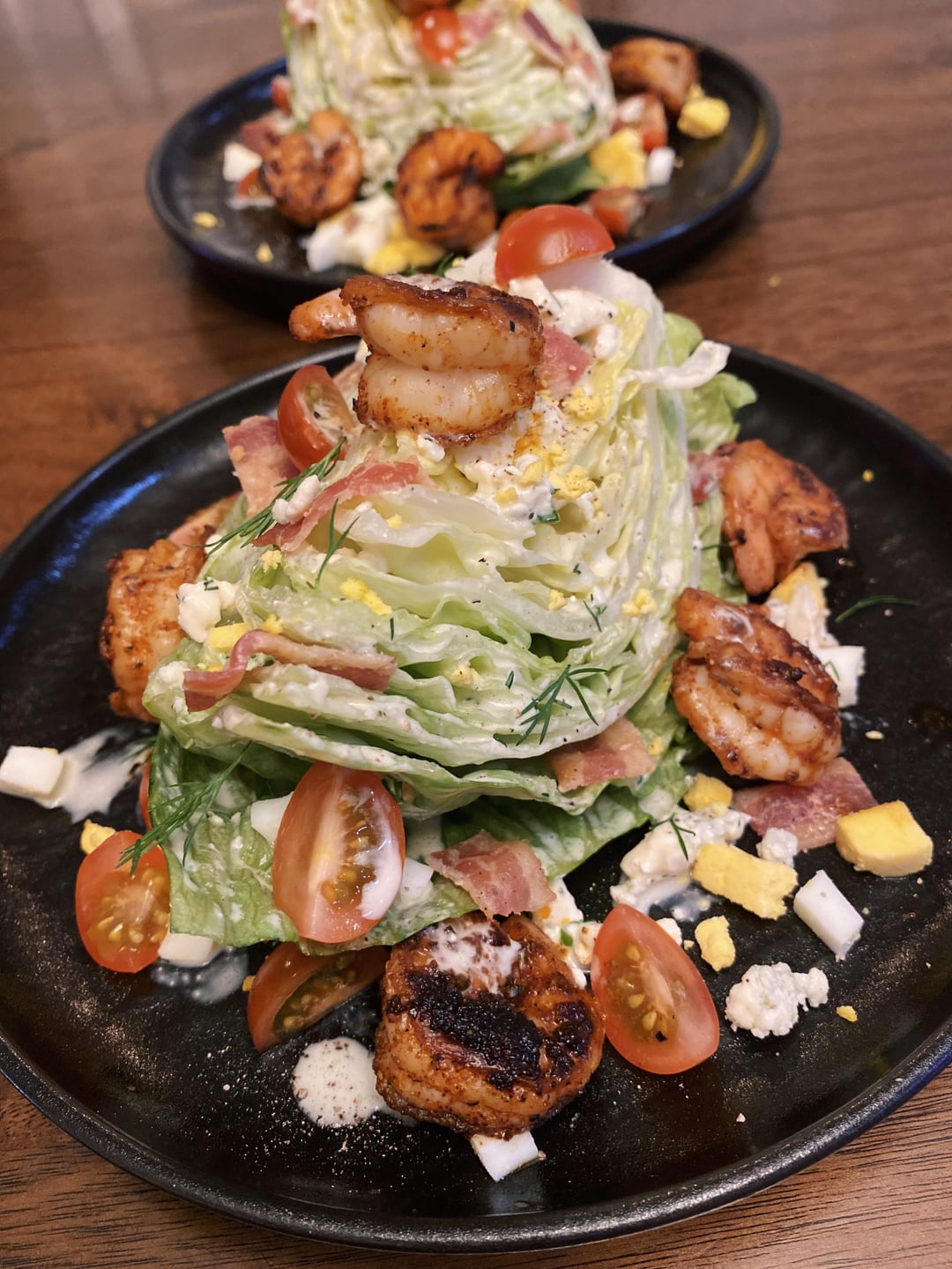 A wedge salad with blackened shrimp, bacon bits, tomatoes, hard boiled