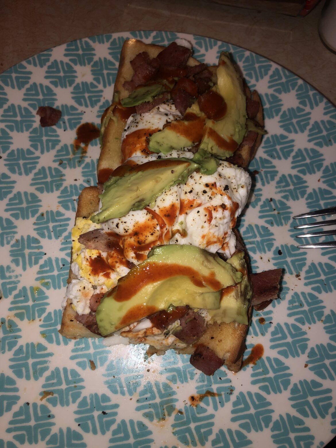 Poached egg on buttered toast with avocado, freshly ground pepper and salt, Tapatio, and diced grilled ham.