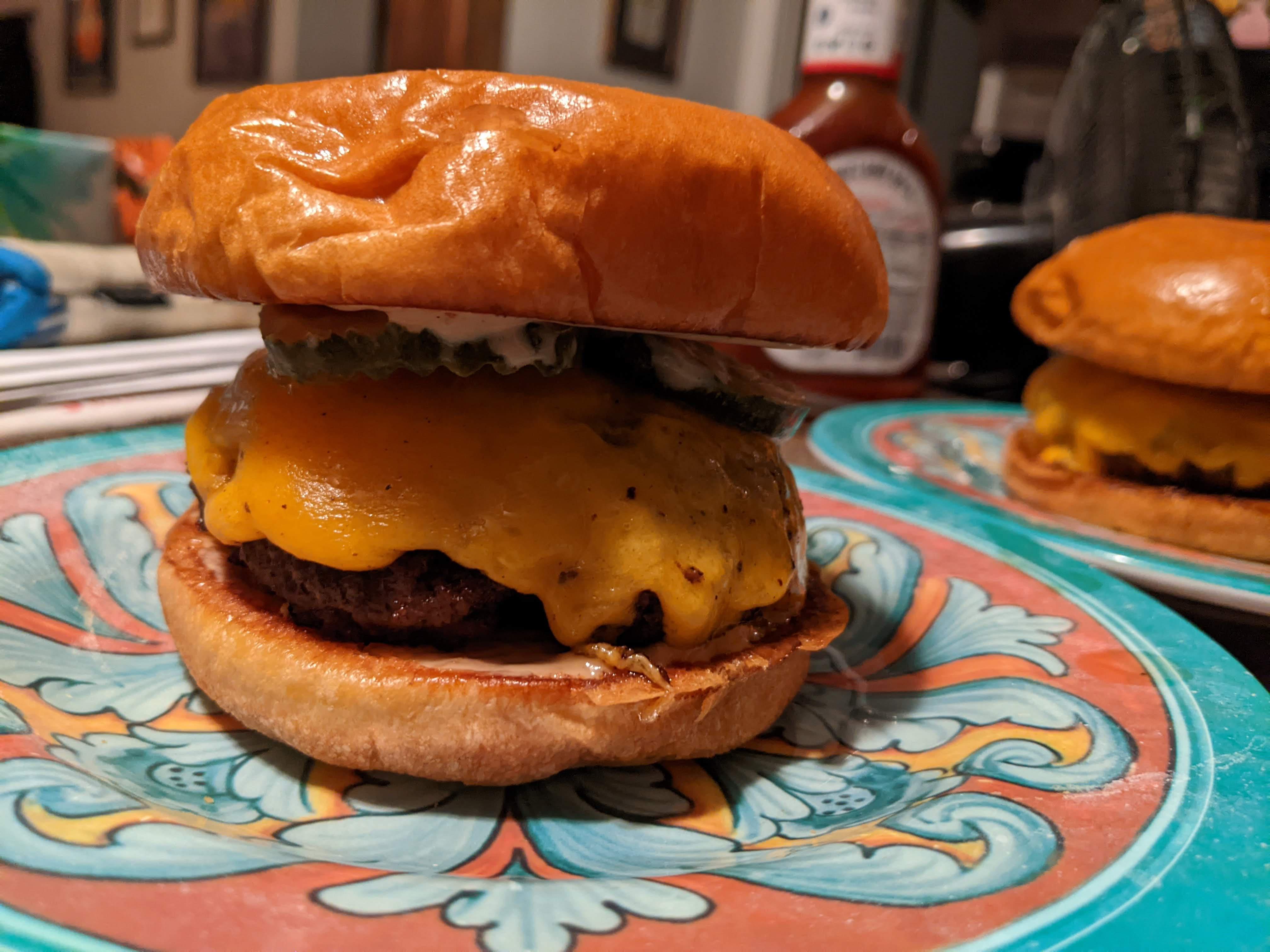 Cast iron cooked burger with cheddar cheese, burger sauce, and dill pickles on a toasted brioche