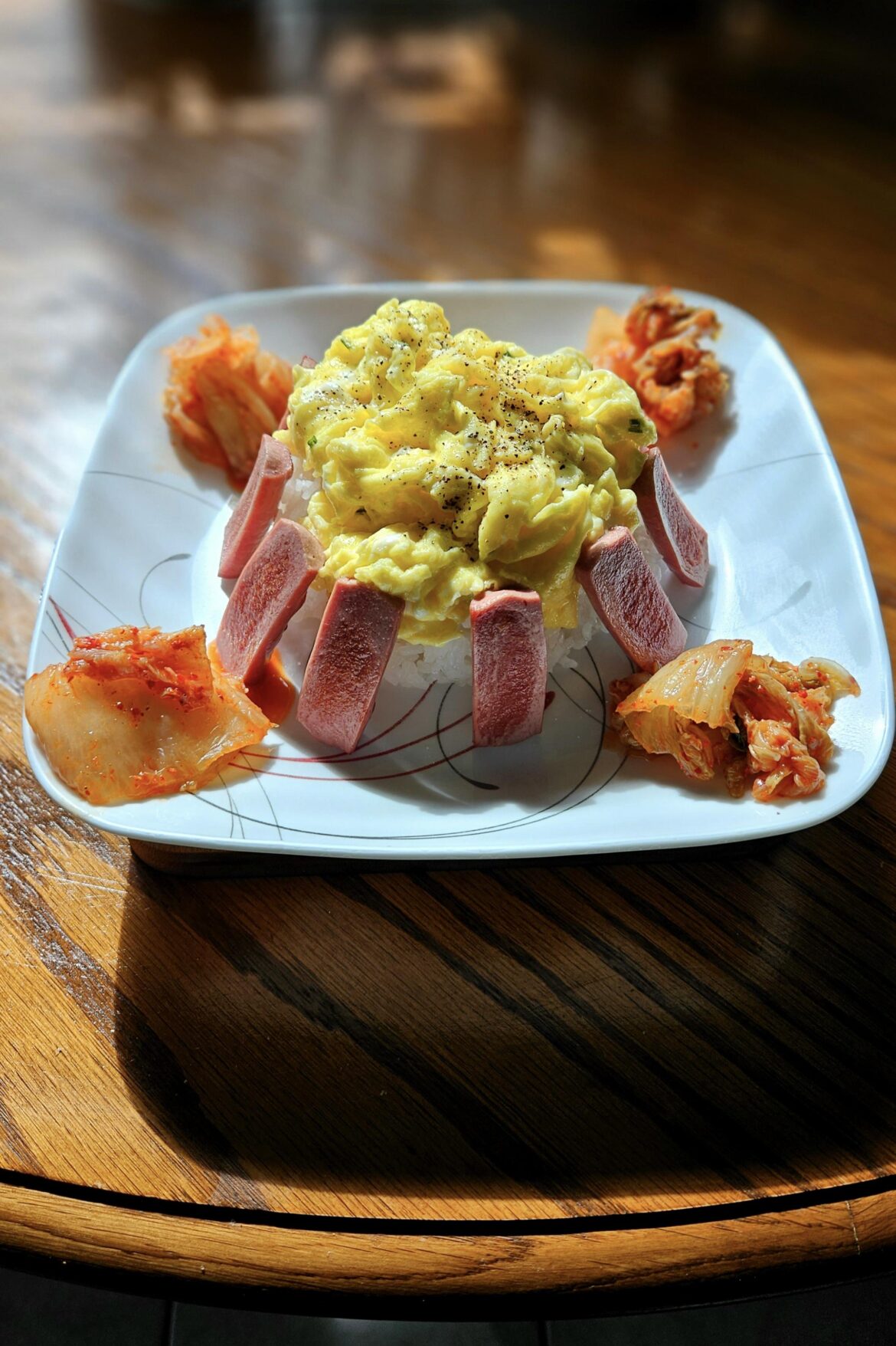 Scrambled eggs on top of steamed rice with Vienna sausage and kimchi.