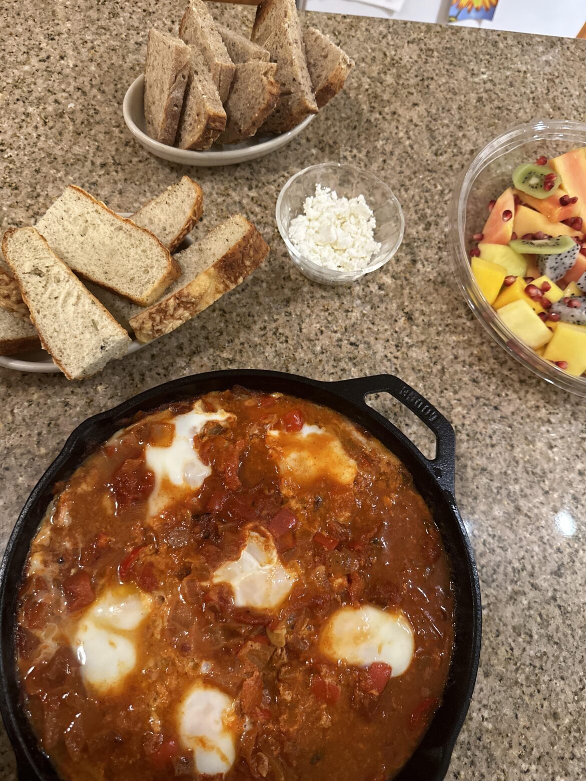 Shakshuka with bread, goat cheese, and a random tropical fruit tray.