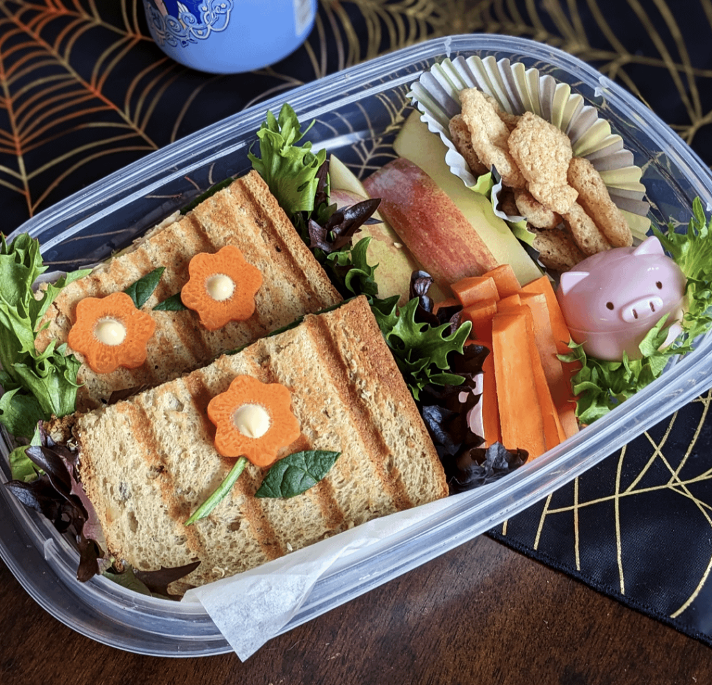 Grilled spicy tuna sandwich, apple slices, carrot sticks, cuttlefish crisps, and a little piggie of sultanas.