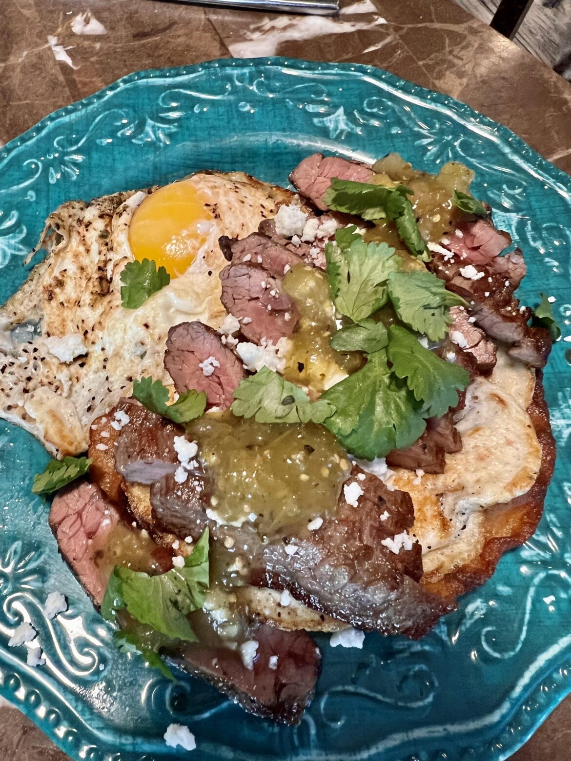 Tostada with skirt steak, queso fresco, green salsa, and a couple fried eggs