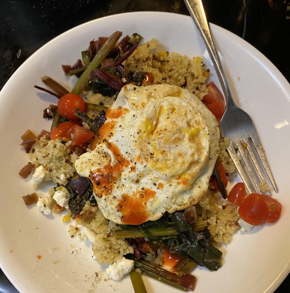 Couscous with veggies, sautéed greens, feta, tomato, and a fried egg - with a little Cholula on top!