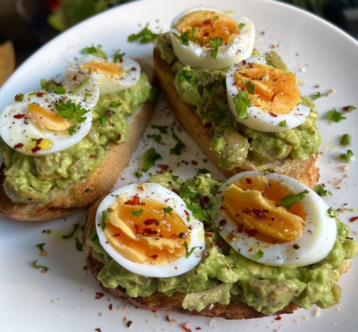 Avocado toast with green olives and lemon juice, topped with boiled eggs and chili.