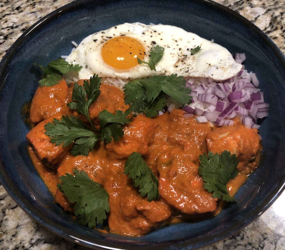 Chicken tikka masala over jeera rice with a sunny side