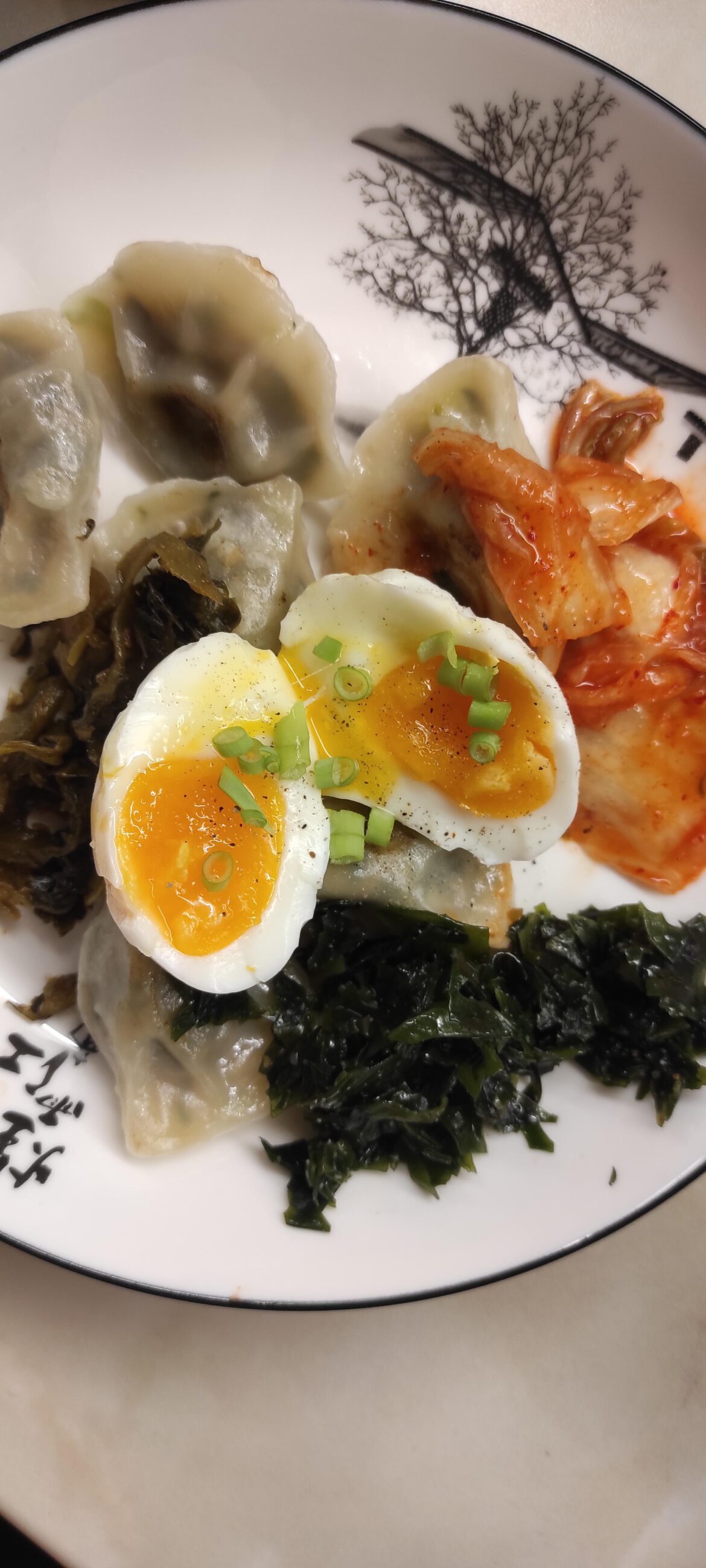 soft boiled egg on potstickers, kimchi, wakame salad and pickled mustard greens