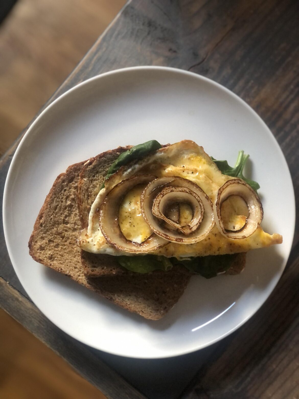 Fried egg sandwich on seedy bread with cheddar cheese, spinach, carmelized onions, and Cholula hot sauce