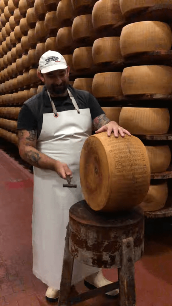 A cheese master using a small hammer to audibly check for any textural anomalies inside a wheel of Parmigiano Reggiano