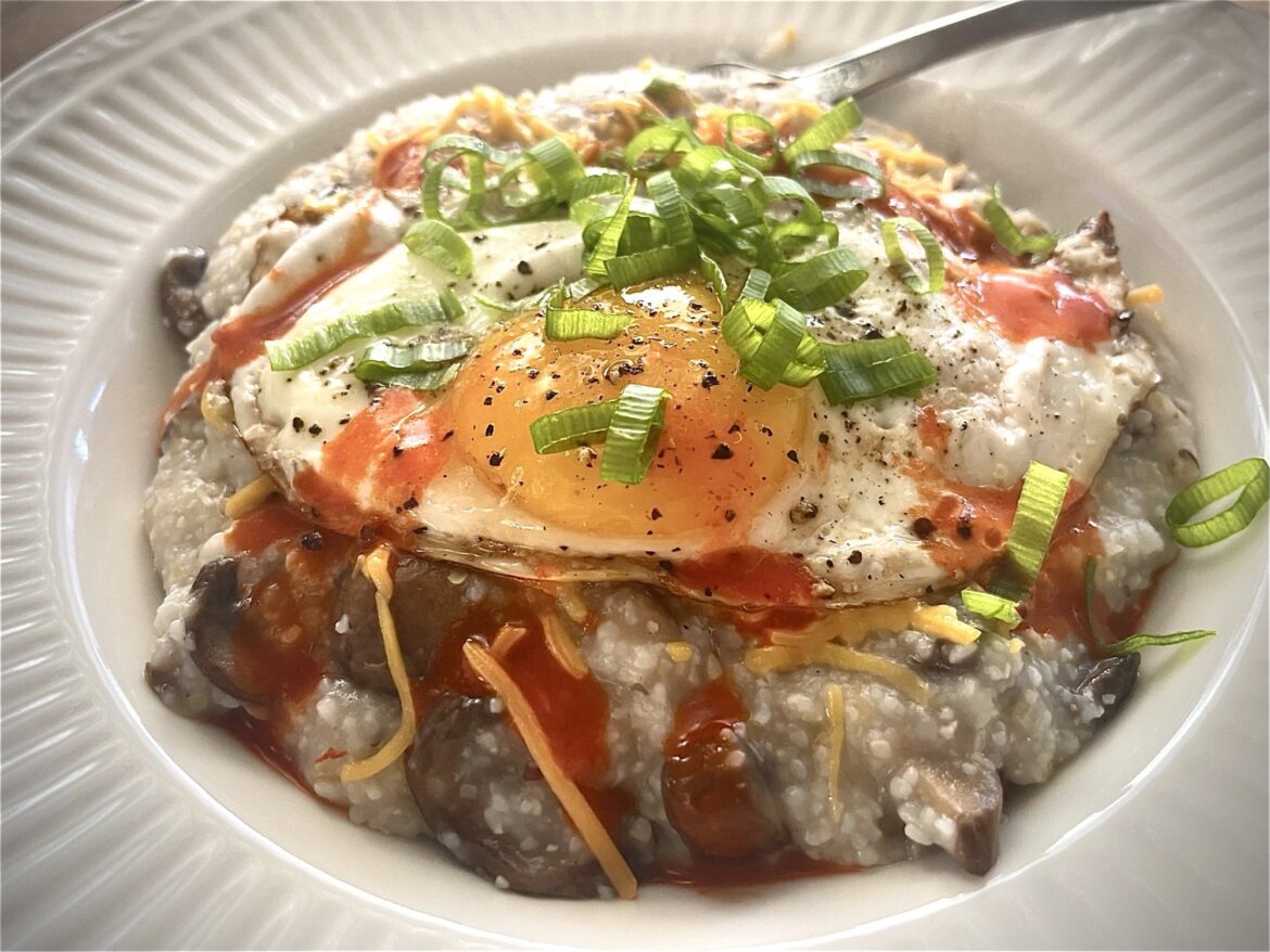 Mushroom grits with cheese topped with a fried egg, scallions, and Cholula!