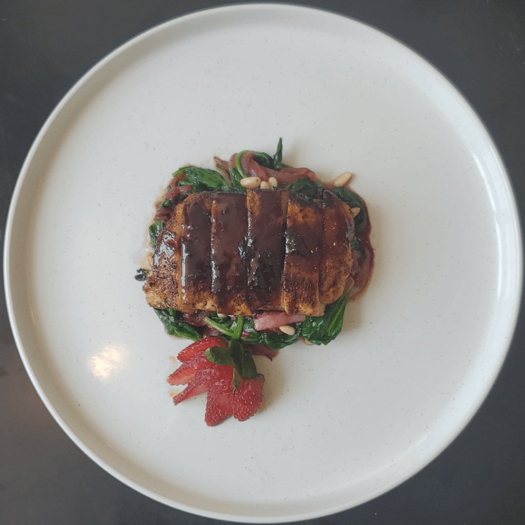 Seared pork tenderloin topped with a red wine pan reduction on wilted spinach with caramelized strawberry and Vidalia onion