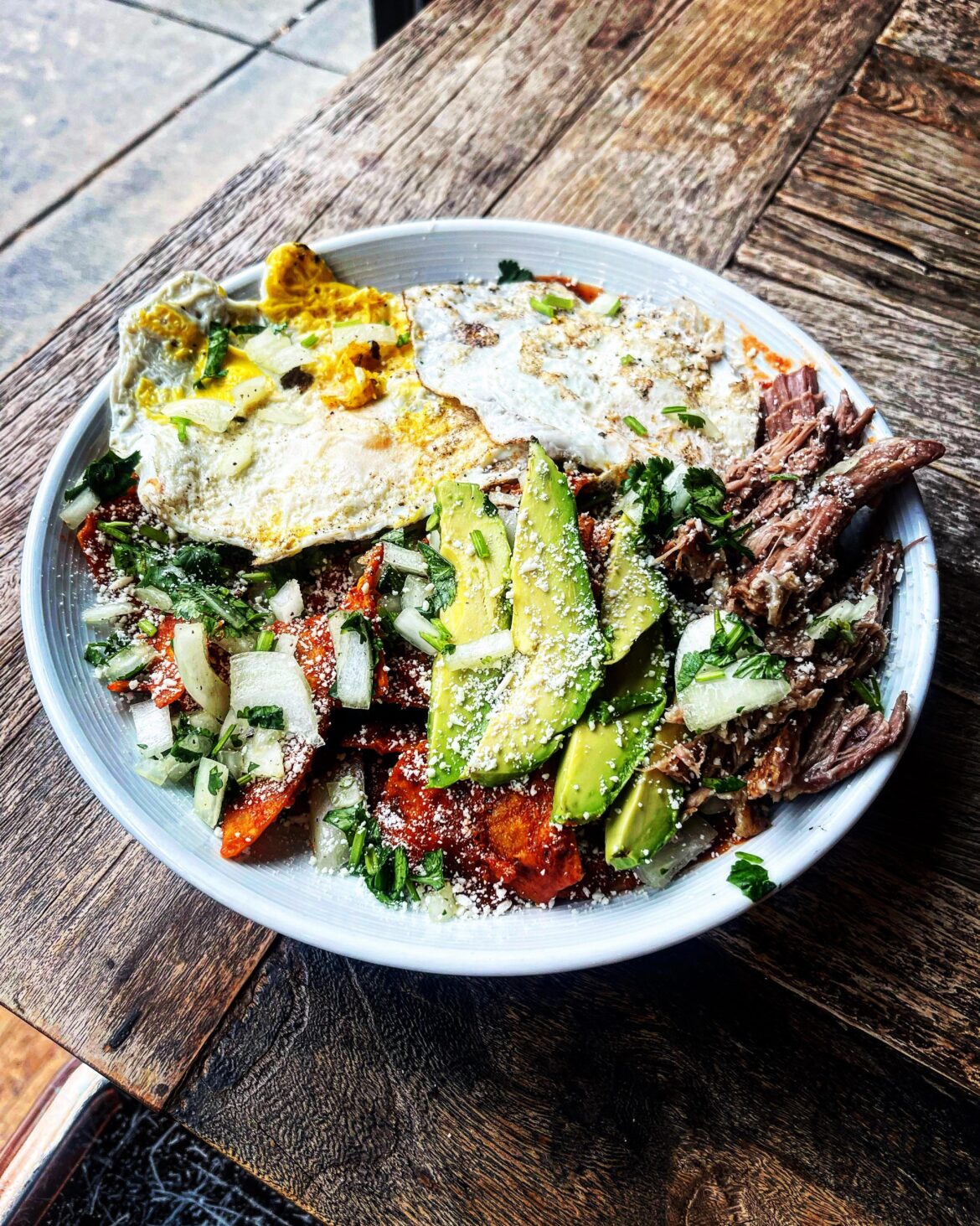 Chilequilas Rojas, corn tortilla chips simmered in guajillo salsa, cerveza braised carnitas, fried egg, avocado, cilantro and white onion treated with lime, cotija cheese (not supposed to be an elegant plating, but damn delicious)