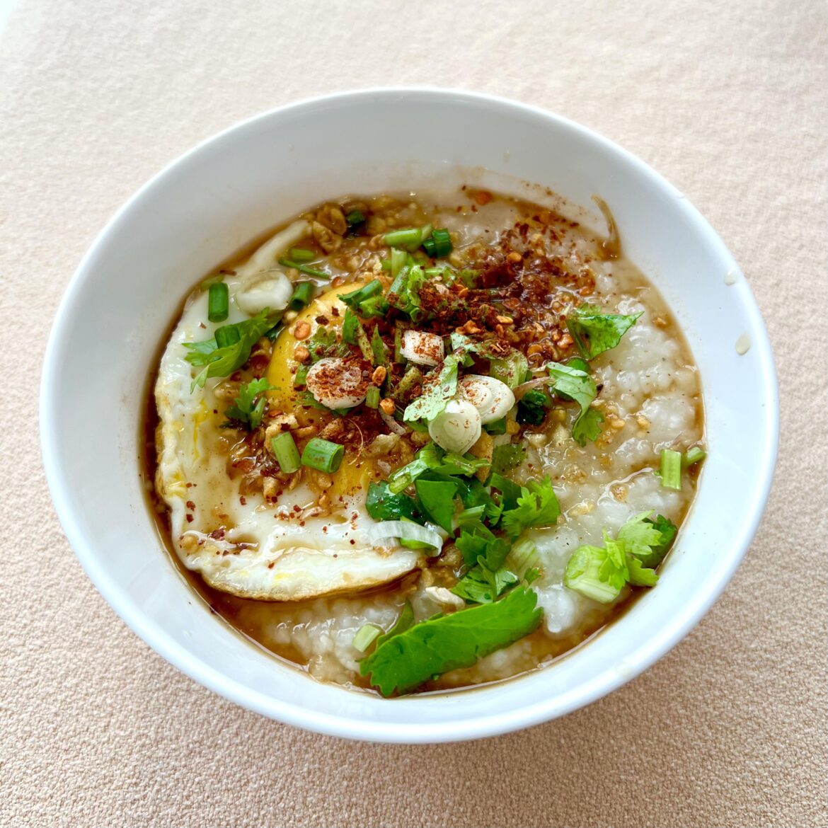 Breakfast mushroom congee with egg, Maggi, herbs, chili and fried garlic in Uthai Thani