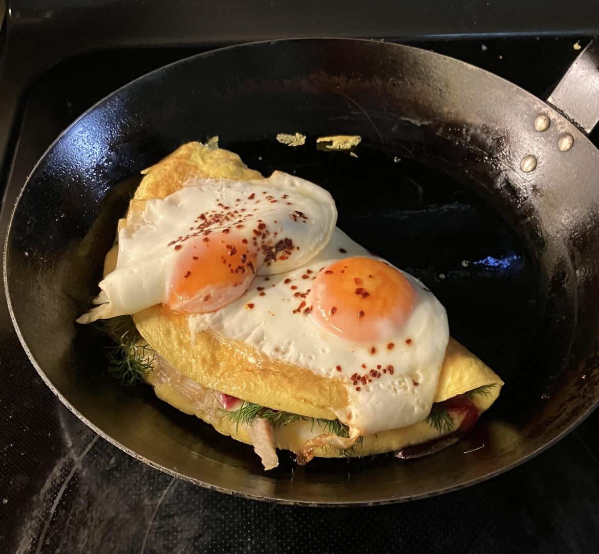 An egg, and another egg, clumsily on a two-egg omelet with smoked salmon, dill and beet-juice pickled onions