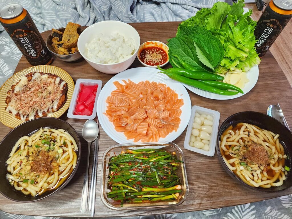 Made dinner in bed for my gf! (Poorly sliced) Salmon, okonomiyaki, udon, homemade green onion kimchi, and Korean Lemon Jin to wash it all down