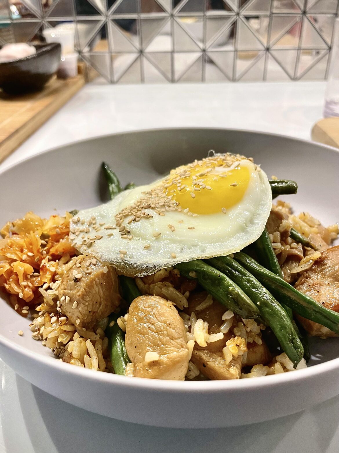 Leftover String bean chicken, egg fried rice, kimchi and an Egg on it with sesame seeds.