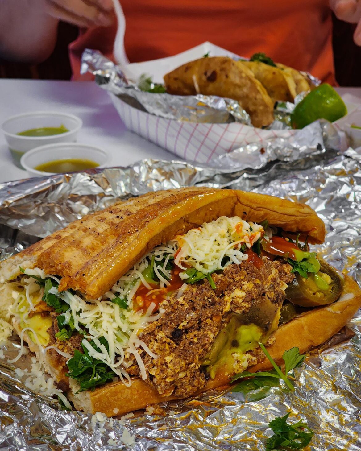 Torta stuffed with chorizo scrambled eggs, avocado, beans, sour cream, cheese, guac sauce, salsa, cheese, jalapeños, cilantro